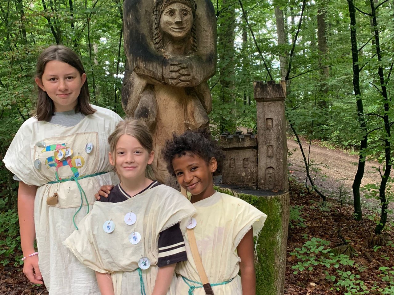 Drei Mädchen in beigen Mittelalterkleider stehen im Wald. 