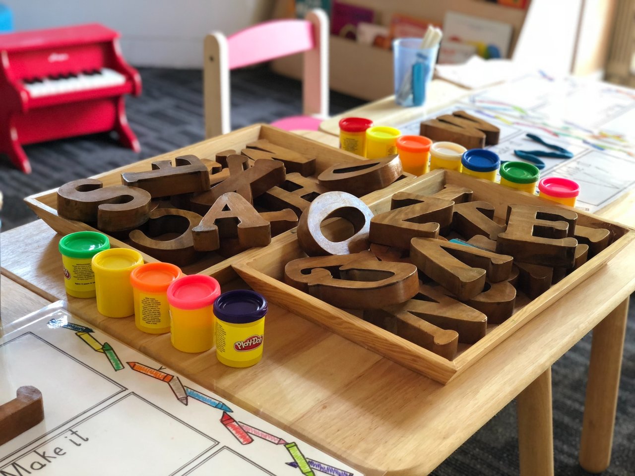 Tisch mit Holzbuchstaben, Knete, im Hintergrund steht ein kleines Spielklavier. 