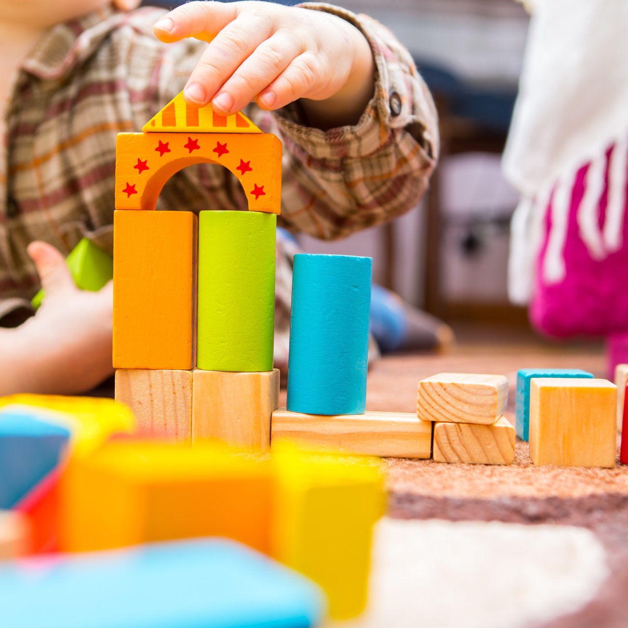 Kind spielt mit farbigen Bauklötzen aus Holz auf dem Boden und baut ein Turm. 